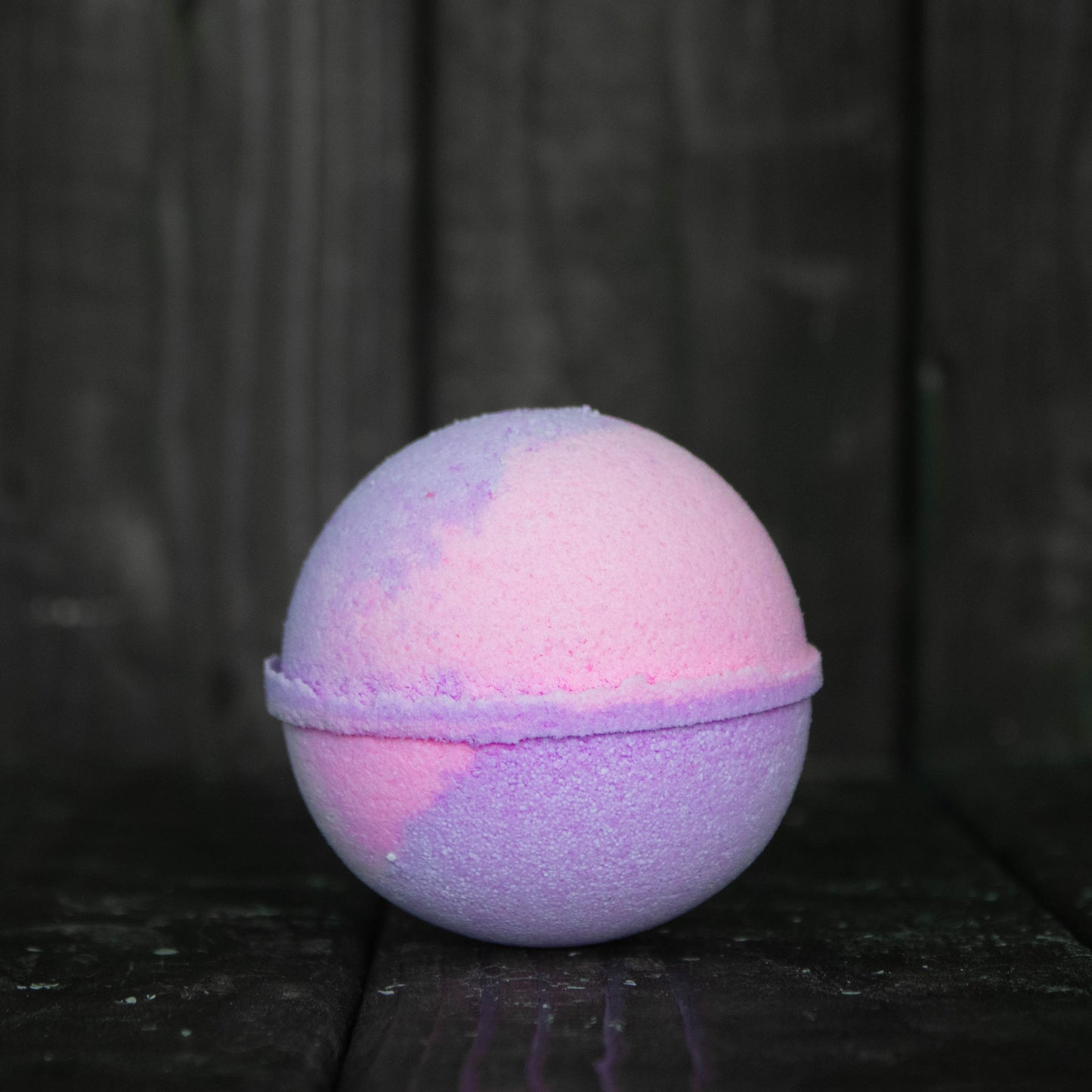A pink and purple bath bomb in front of a dark wood background.