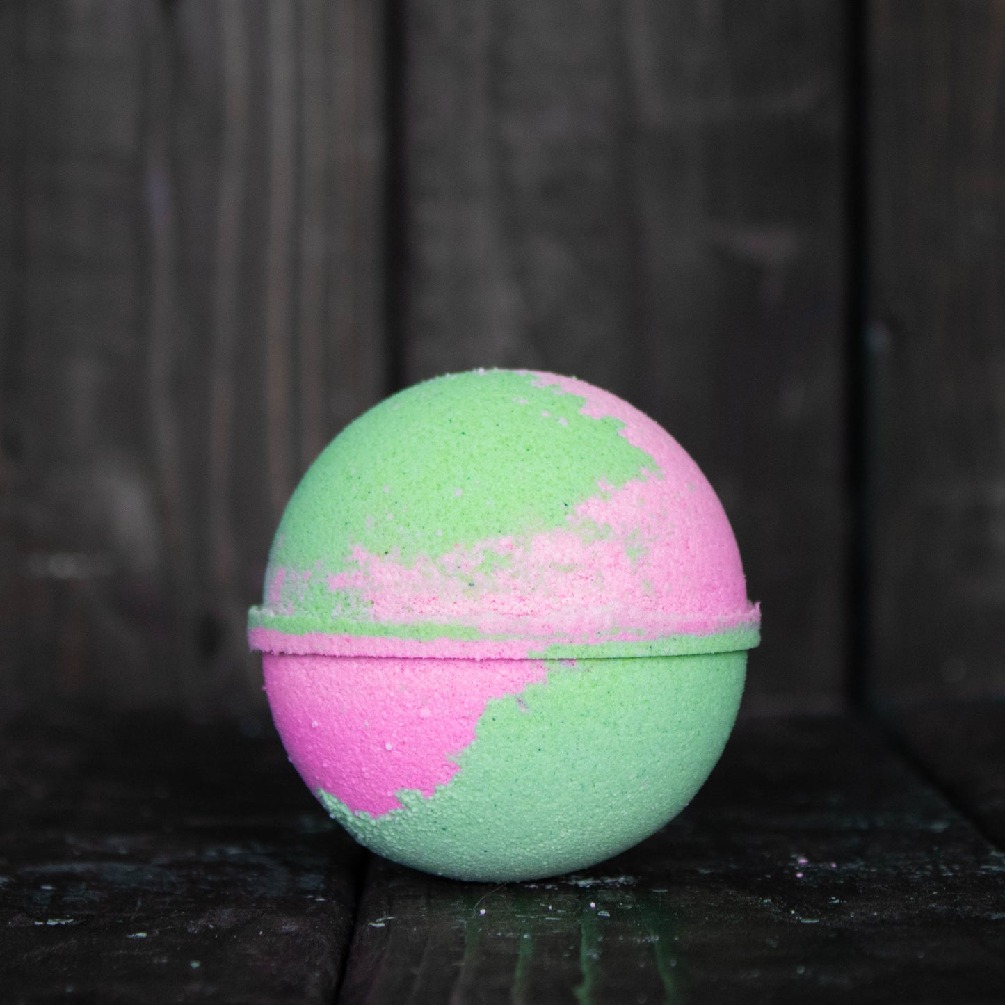 A green and pink bath bomb in front of a dark wood background.