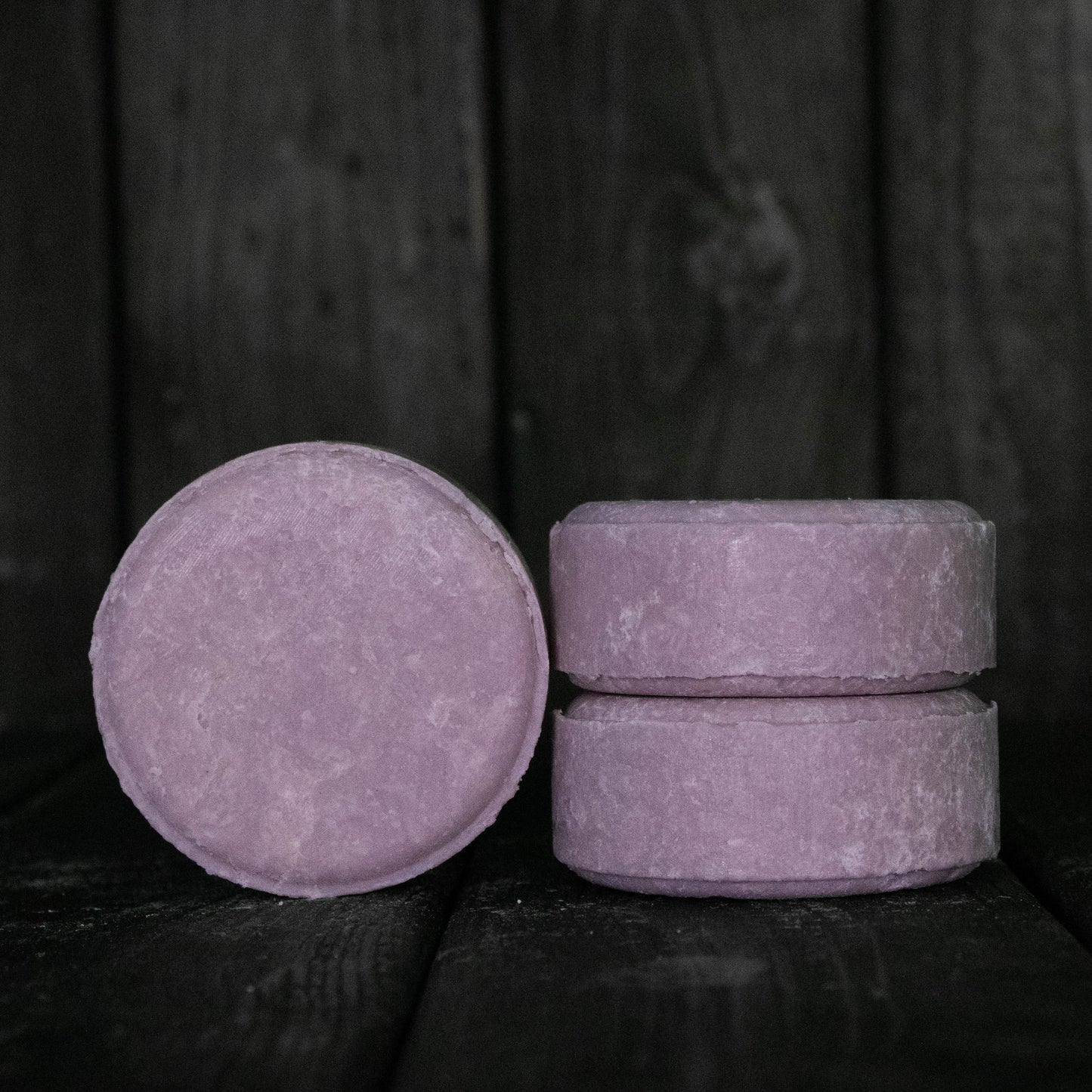 A round purple shampoo bar next to a stack of two purple shampoo bars.