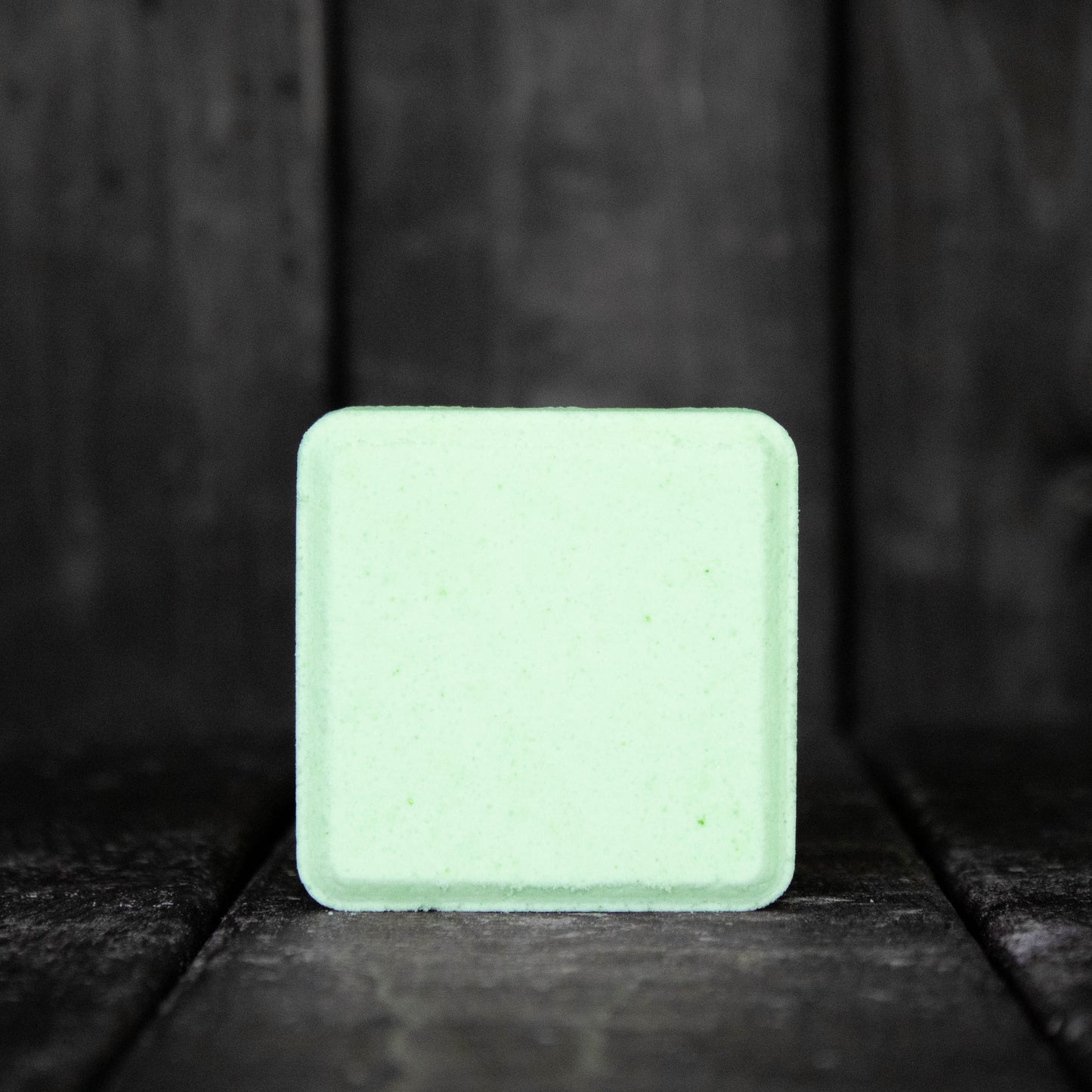 A light green, square shaped shower steamer in front of a dark wood background.