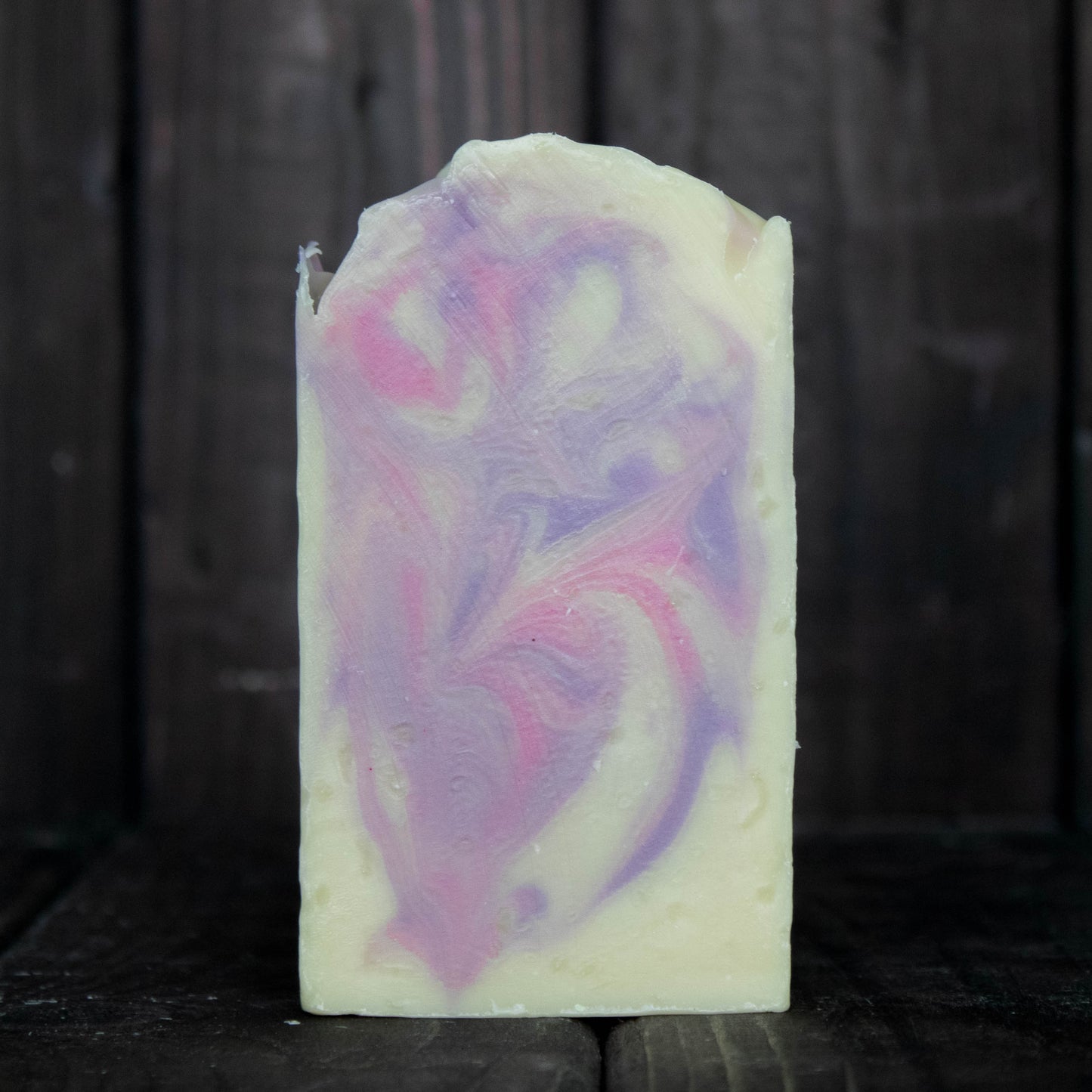 Soap with pink and purple swirls in front of a dark wood background.