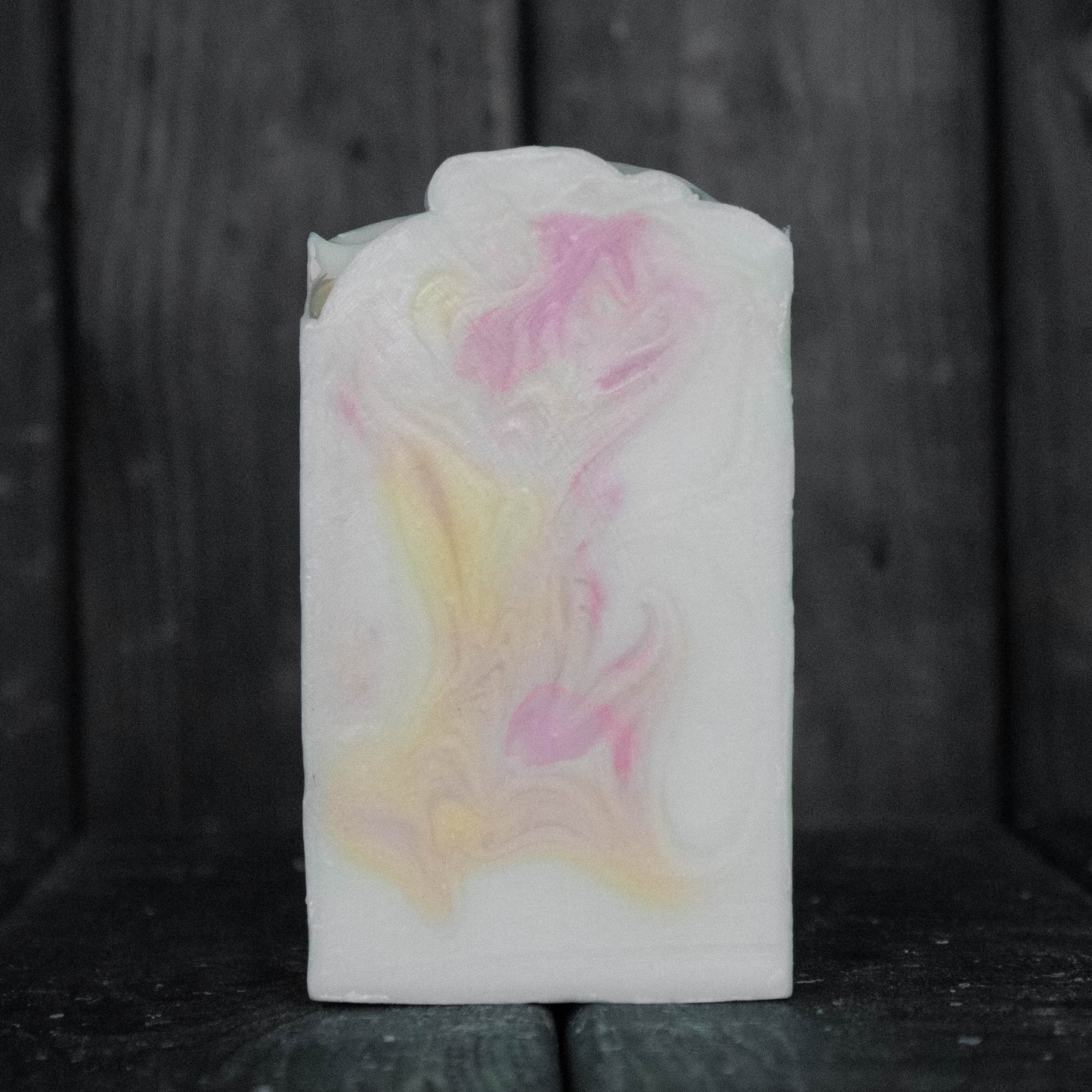 Soap with pink and yellow swirls in front of a dark wood background.