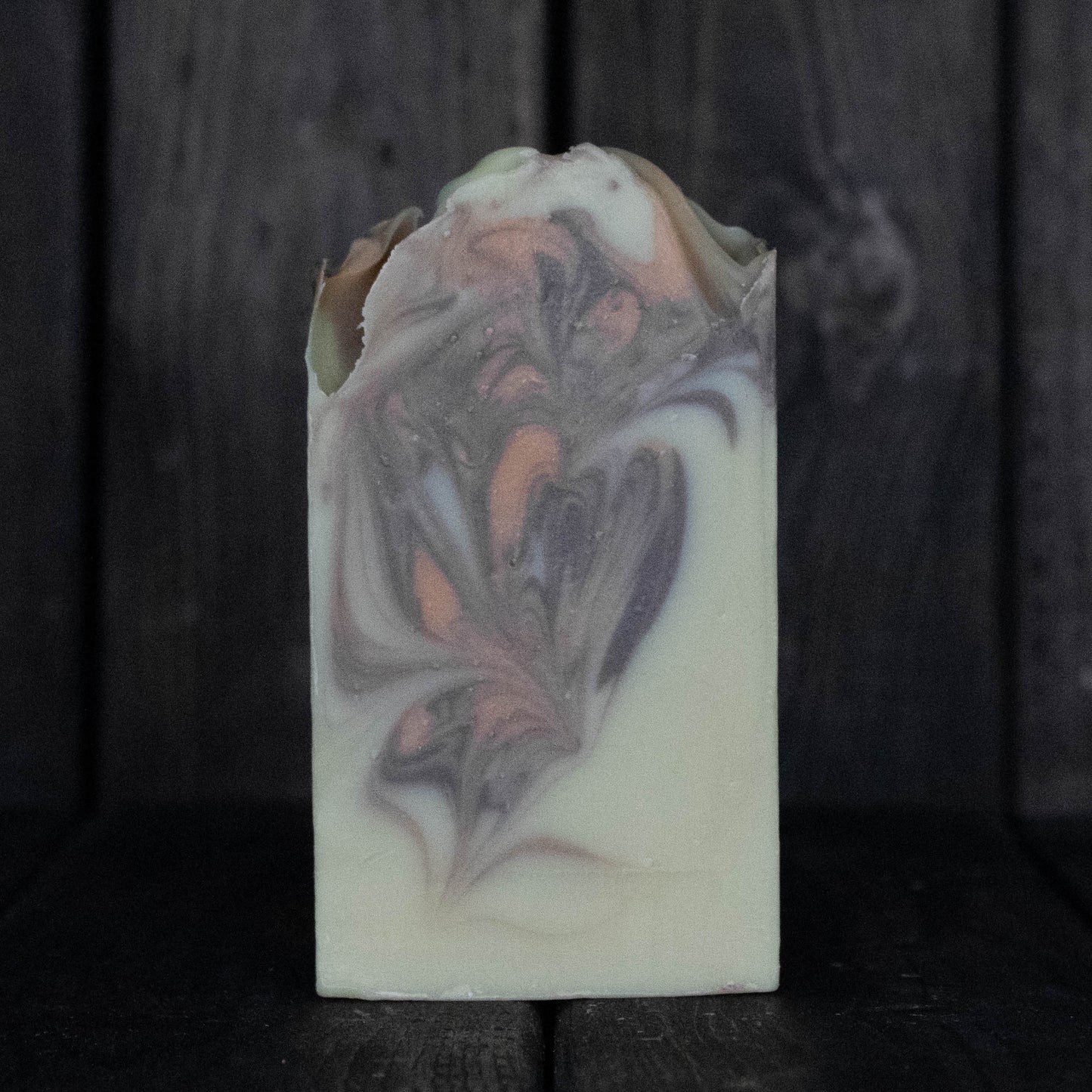 Soap with brown and orange swirls in front of a dark wood background.