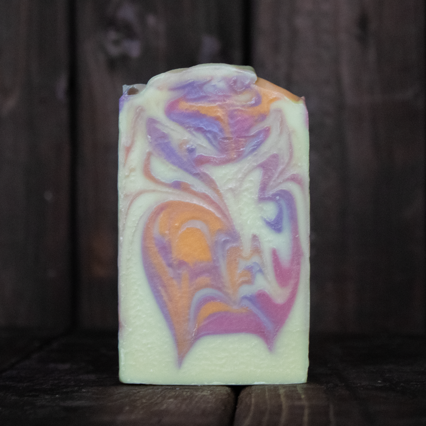 Soap with orange, coral, and purple swirls in front of a dark wood background.