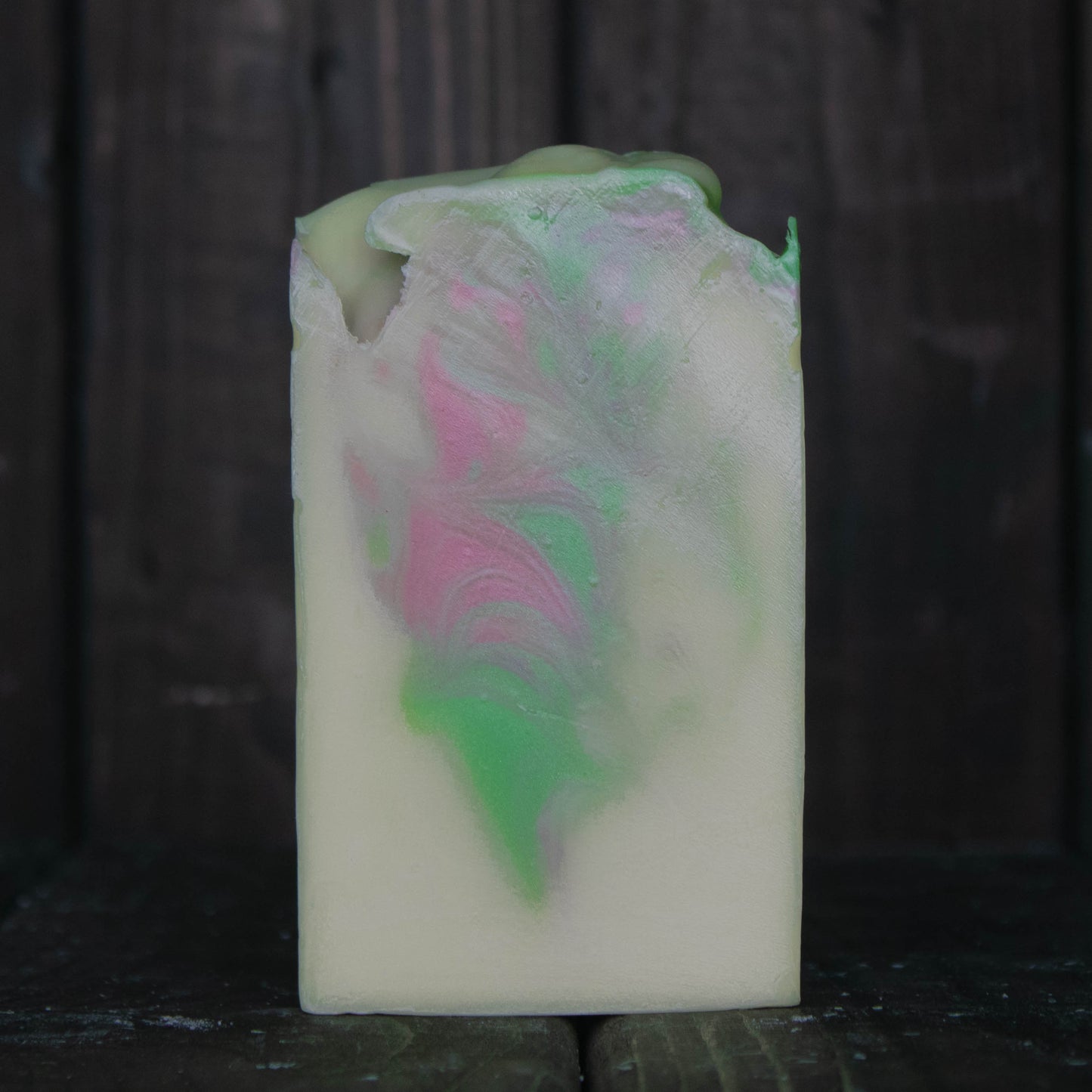 Soap with green and pink swirls in front of a dark wood background.