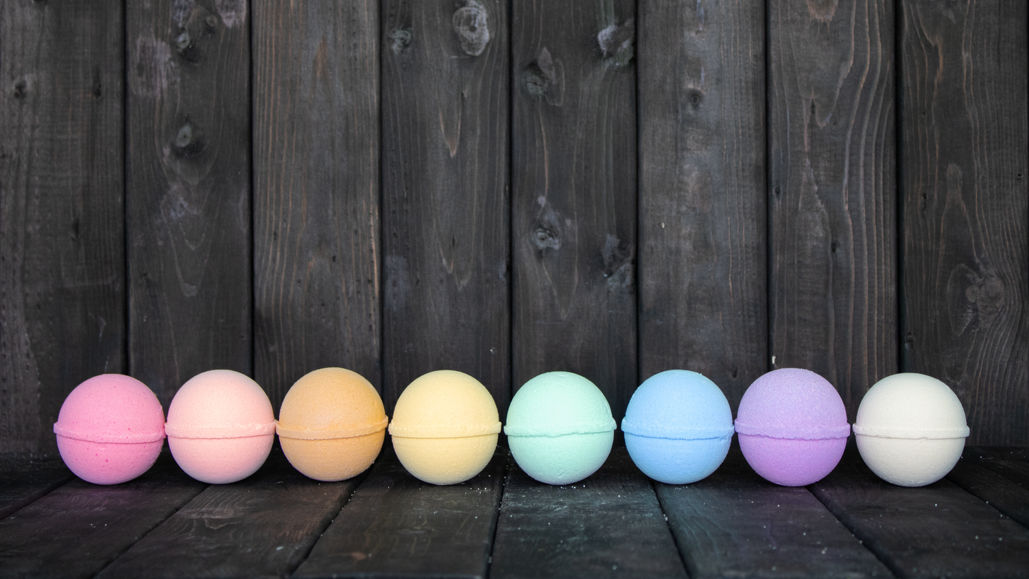 Colourful bath bombs in front of a dark wood background.