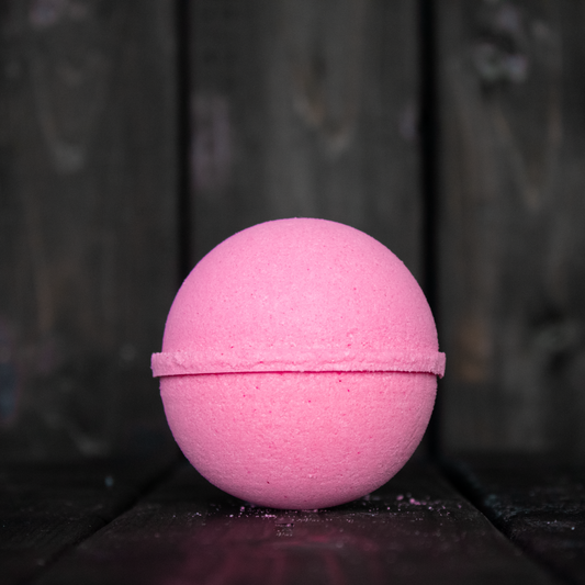 A pink bath bomb in front of a dark wood background.