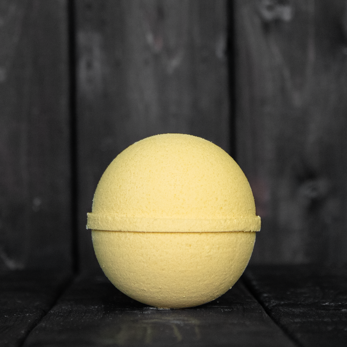 A yellow bath bomb in front of a dark wood background.