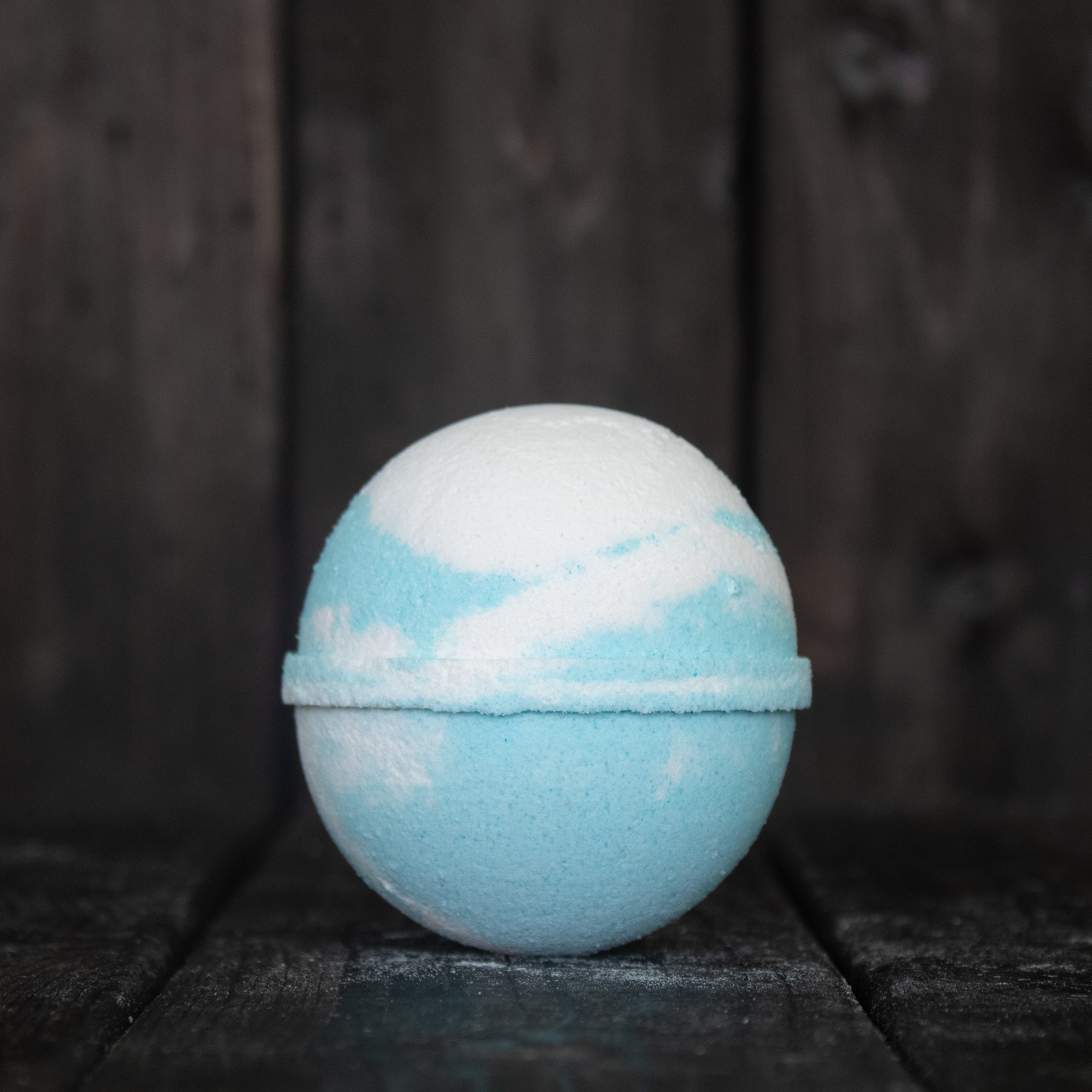 A blue and white bath bomb in front of a dark wood background.