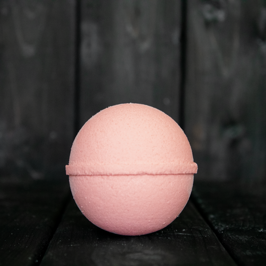 A peach coloured bath bomb in front of a dark wood background.