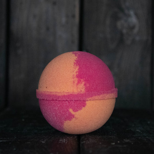 A red and orange bath bomb in front of a dark wood background.