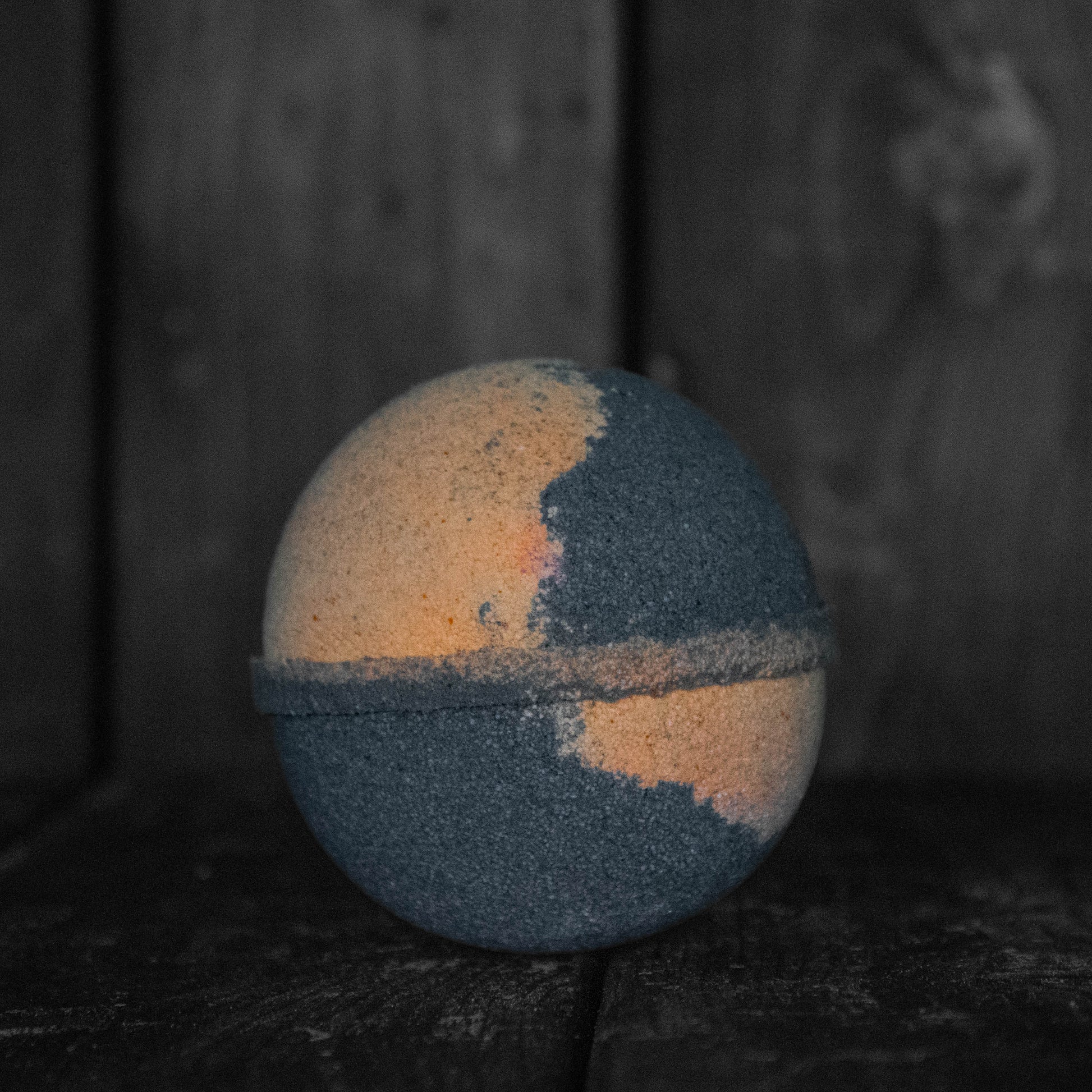 A black and orange bath bomb in front of a dark wood background.