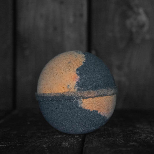 A black and orange bath bomb in front of a dark wood background.