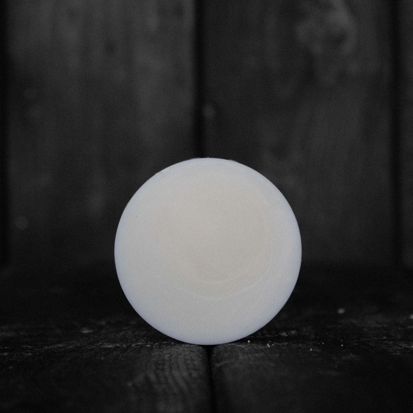 A round cream coloured conditioner bar in front of a dark wood background.