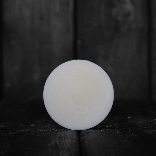 A round cream coloured conditioner bar in front of a dark wood background.