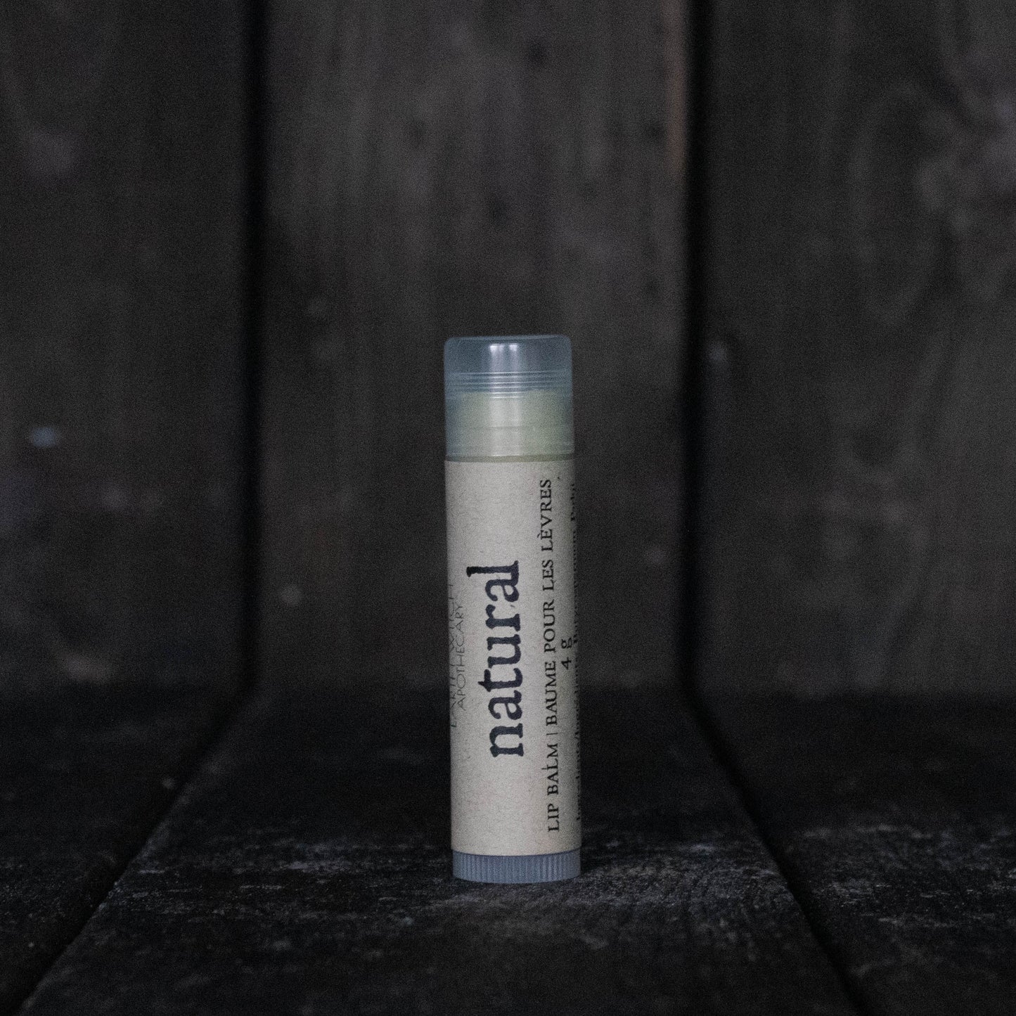 A lip balm tube labelled "Natural" in front of a dark wood background.