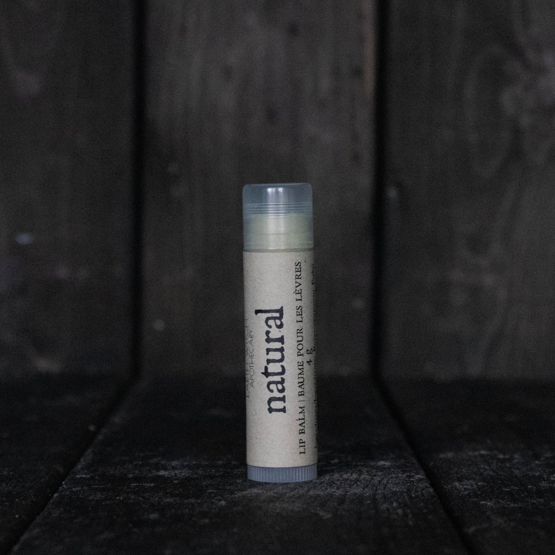 A lip balm tube labelled "Natural" in front of a dark wood background.