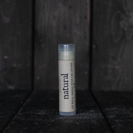 A lip balm tube labelled "Natural" in front of a dark wood background.