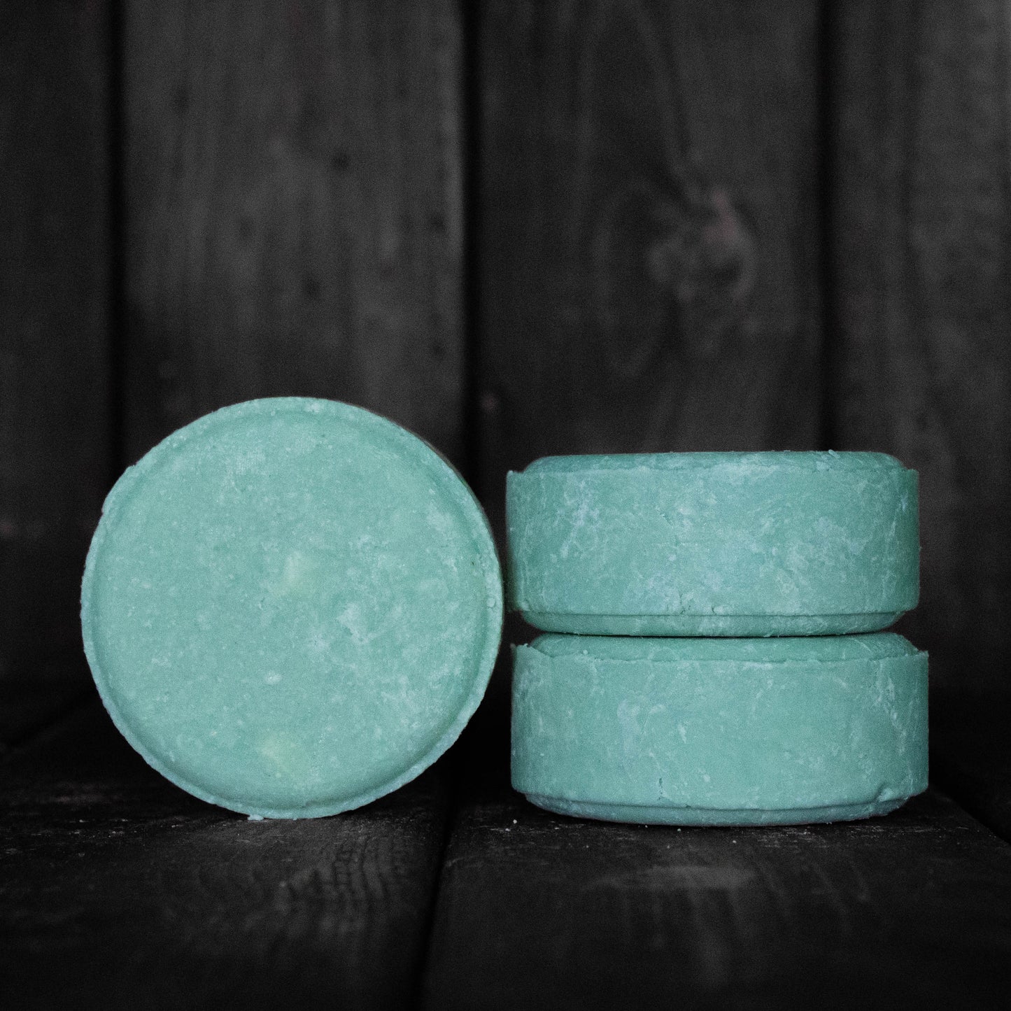 A round turquoise shampoo bar next to a stack of two turquoise shampoo bars.