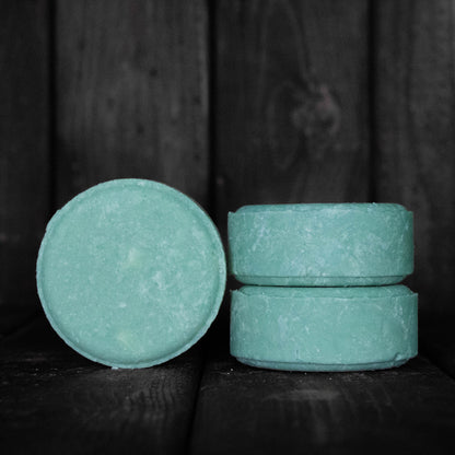 A round turquoise shampoo bar next to a stack of two turquoise shampoo bars.