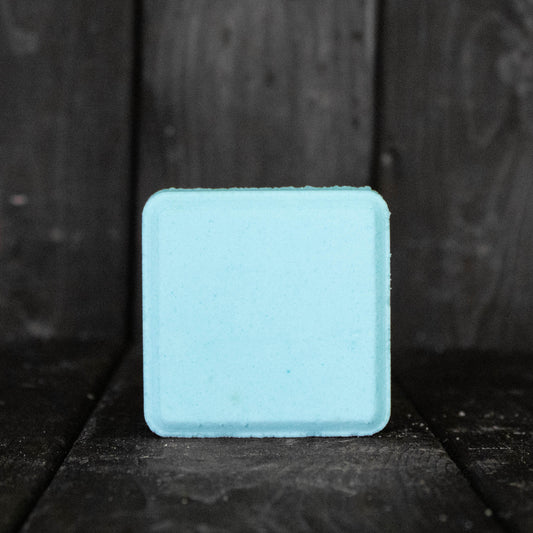 A light blue, square shaped shower steamer in front of a dark wood background.