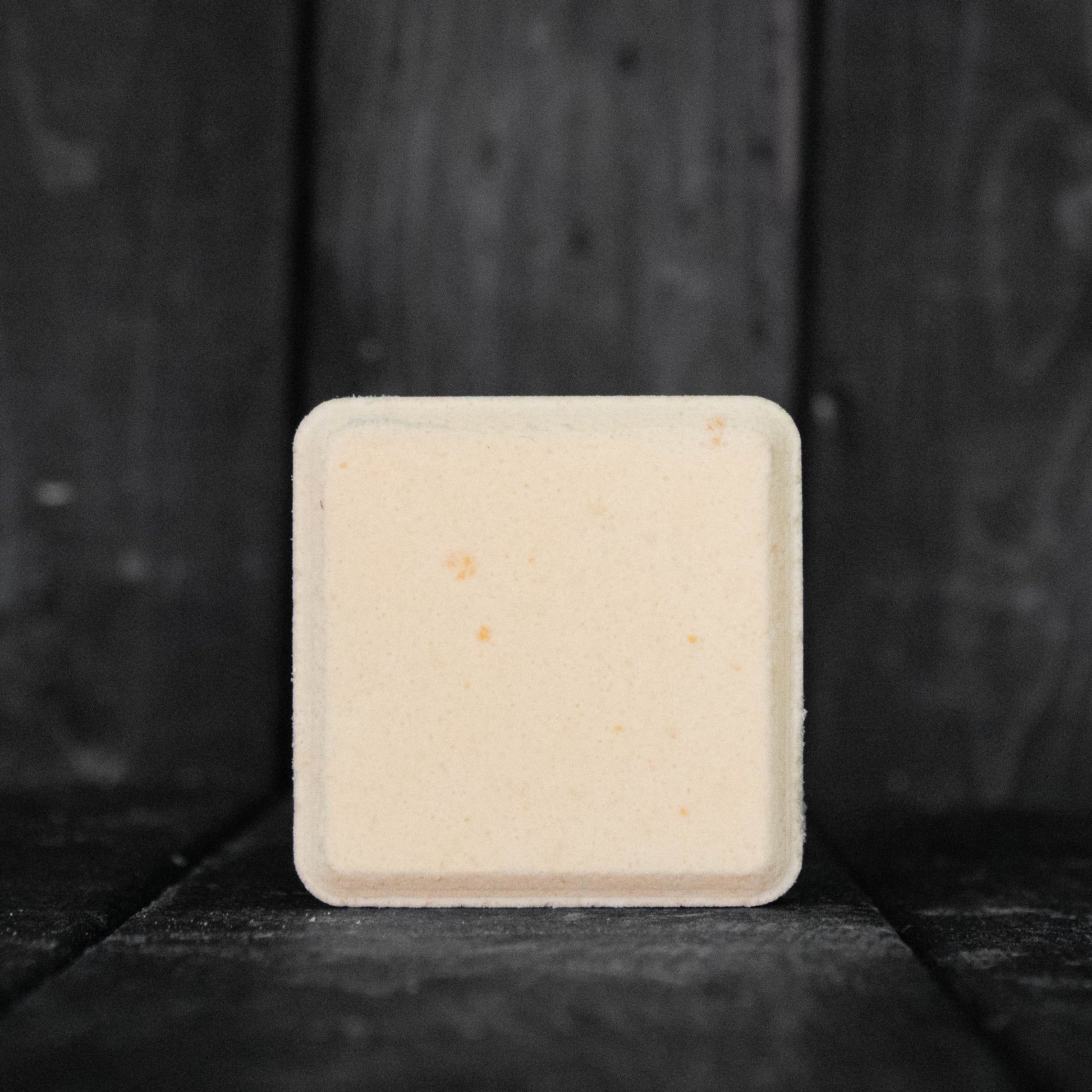 A light orange, square shaped shower steamer in front of a dark wood background.