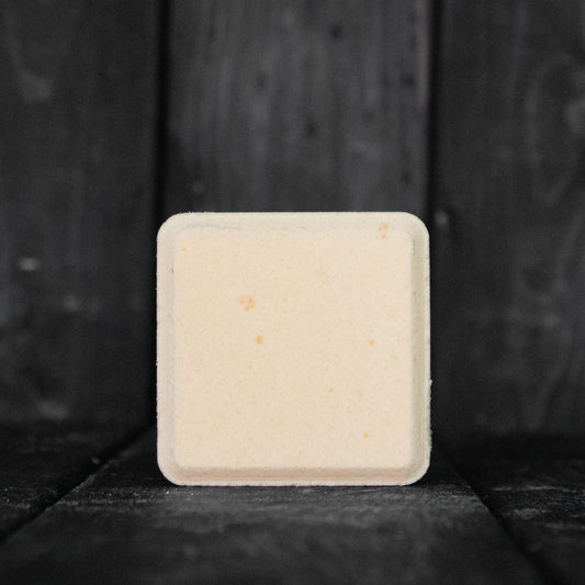 A light orange, square shaped shower steamer in front of a dark wood background.