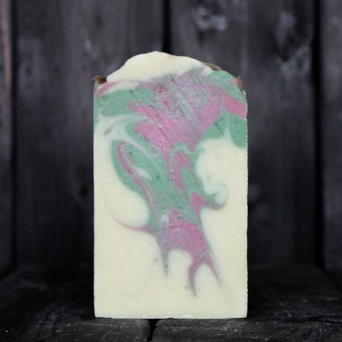 Soap with red and green swirls in front of a dark wood background.