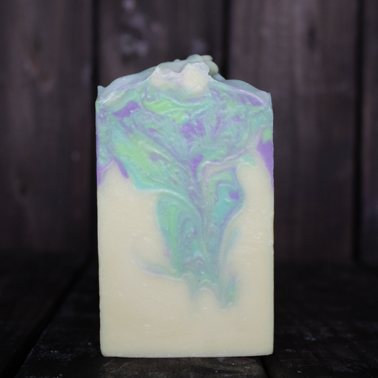 Soap with turquoise, green, and purple swirls in front of a dark wood background.