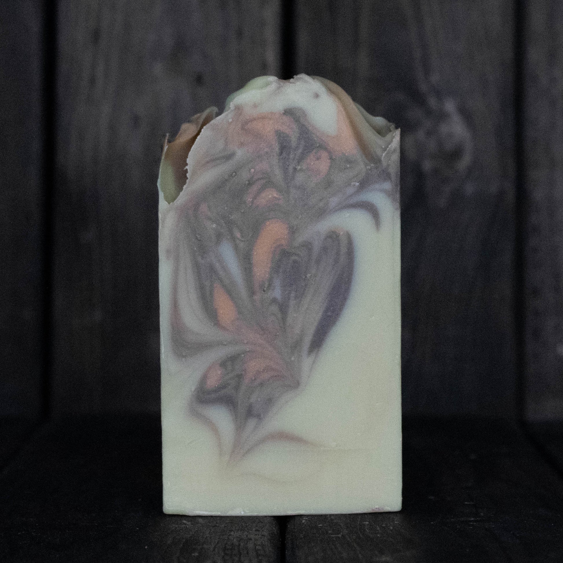 Soap with brown and orange swirls in front of a dark wood background.
