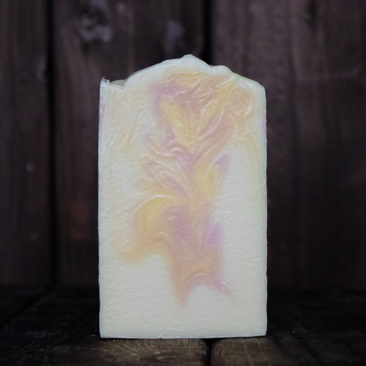 Soap with peach, yellow, and pink swirls in front of a dark wood background.