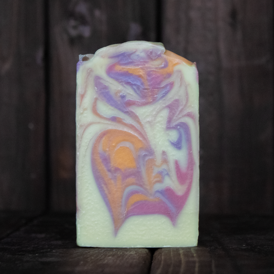 Soap with orange, coral, and purple swirls in front of a dark wood background.